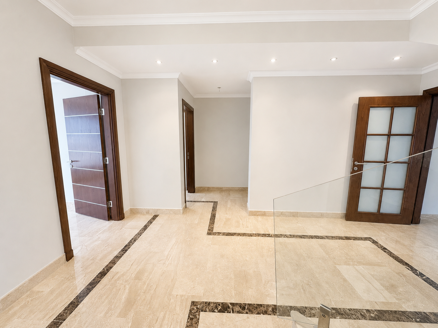 22dc3d1d-8999-4d82-a2f2-81fa0fc732f7 Bright modern hallway with beige marble floors, white walls, and dark wood doors; glass railing on the right.