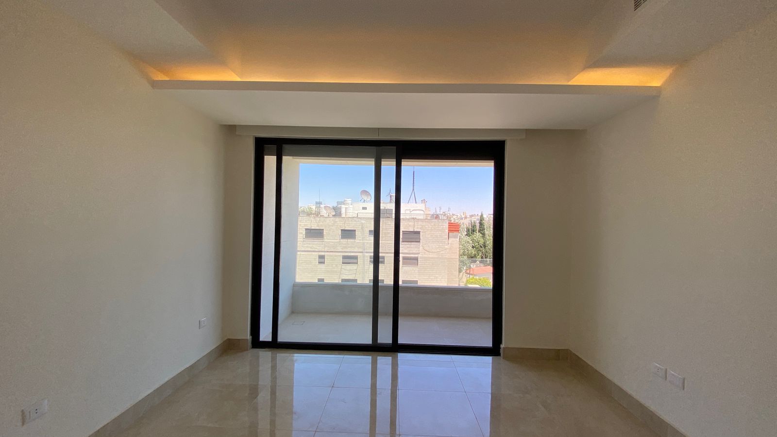 2338dfca-4b4e-403c-8edf-595f7a6f75ae Empty living room with glossy tile floor and a large sliding glass door opening to a balcony with a cityscape view.