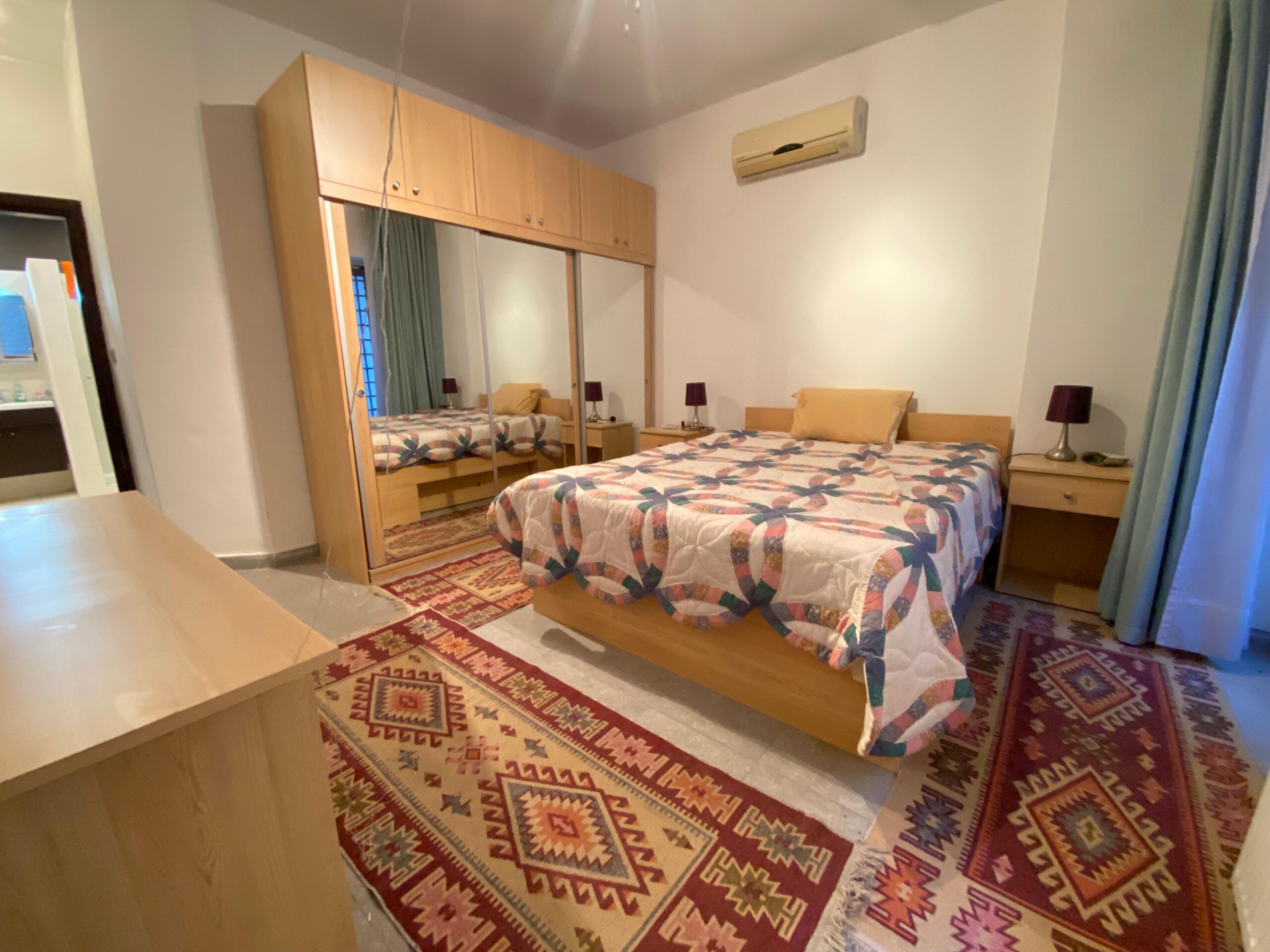 29dd3430-a470-44f7-a33c-c6004c6c232f Bedroom with two single beds, matching wooden furniture, mirrored wardrobe, and a red geometric rug underfoot.