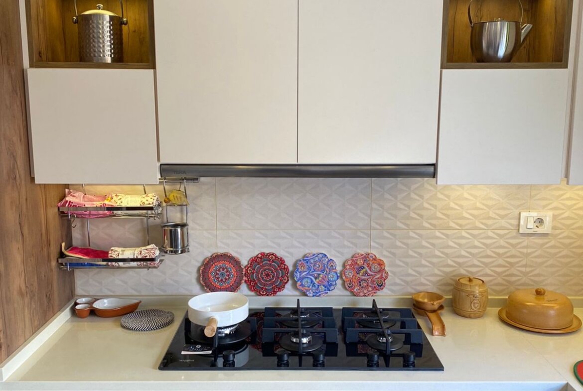 Modern kitchen with white upper cabinets, wooden lower cabinets, and a gas stove; decorative plates on the backsplash and kettles in shelves.