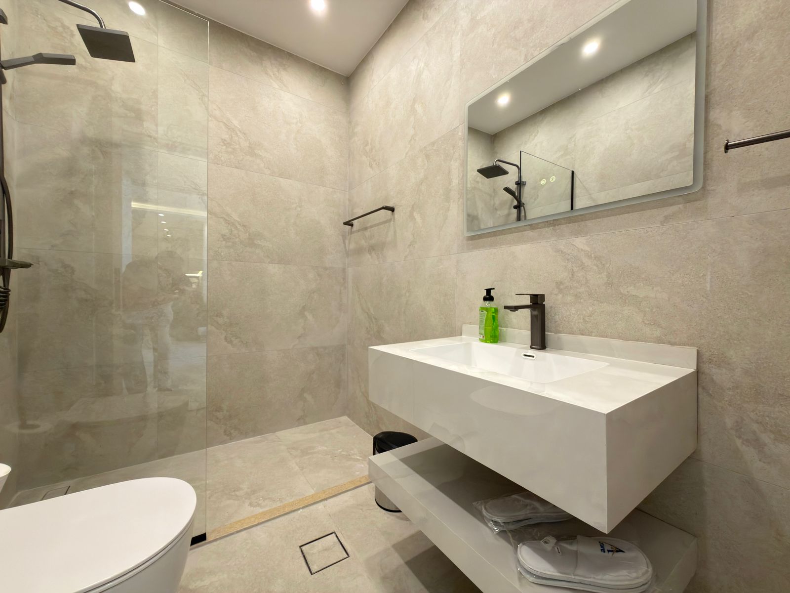 2bf7a29b-6b41-49b7-b22a-0032f2d172e9 Modern bathroom with a glass-walled shower, gray tiled walls, and a white floating vanity with a black faucet and mirror.