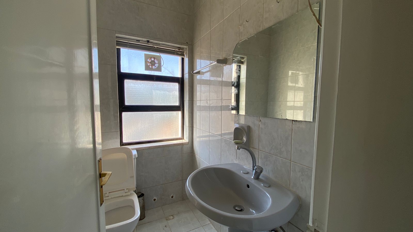 36eb0536-62f8-4679-bafa-8b89c7113d91 Small tiled bathroom with a pedestal sink, toilet, and a frosted window letting in light; mirrors above the sink and a towel rail nearby.