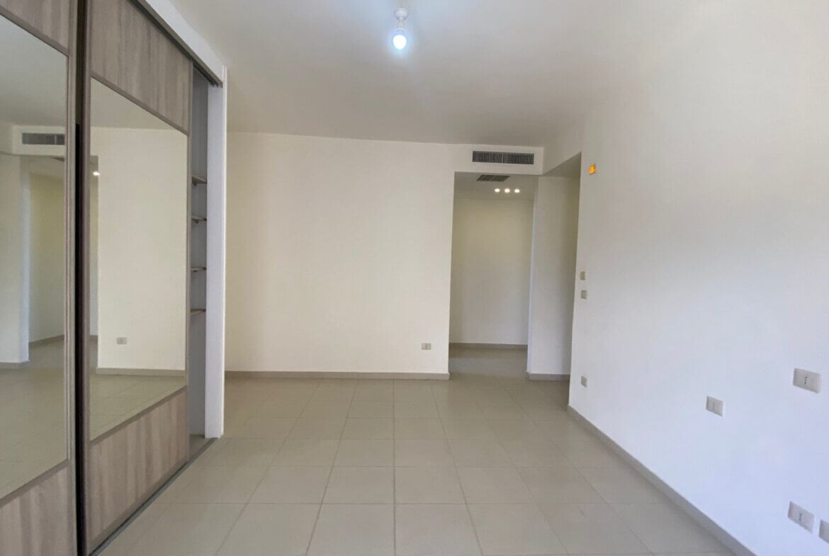 378b4c02-1e76-4374-9556-820f14e5d5ce Empty living room with a built-in wardrobe showcasing mirrored sliding doors on the left and light tiled flooring.