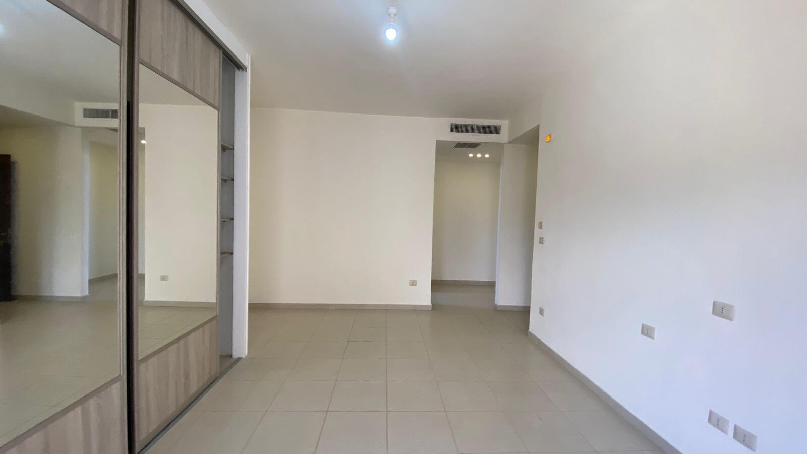 378b4c02-1e76-4374-9556-820f14e5d5ce Empty living room with a built-in wardrobe showcasing mirrored sliding doors on the left and light tiled flooring.