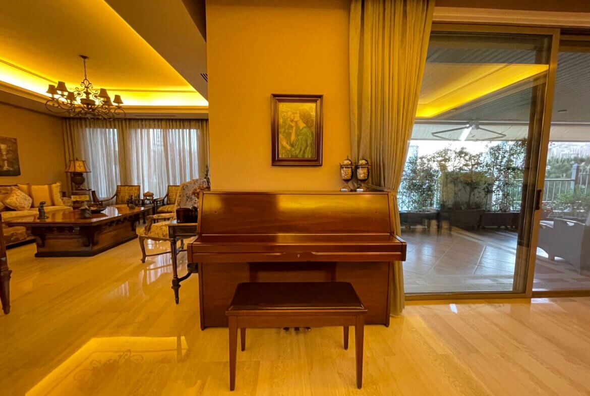 381179a3-aa6f-4f17-8e07-ccd5c9a8dc4c Upright wooden piano at center of a warmly lit living room, with a bench and a painting on the wall behind it, and a balcony door to the right.