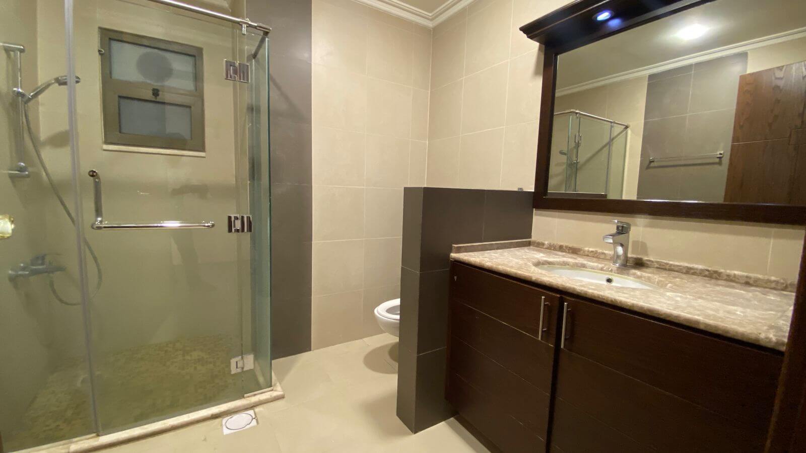 3b6fb577-706b-4d51-ad65-237ff6d267fe Modern bathroom with glass-enclosed shower, dark wood vanity, and marble countertop mirror above.