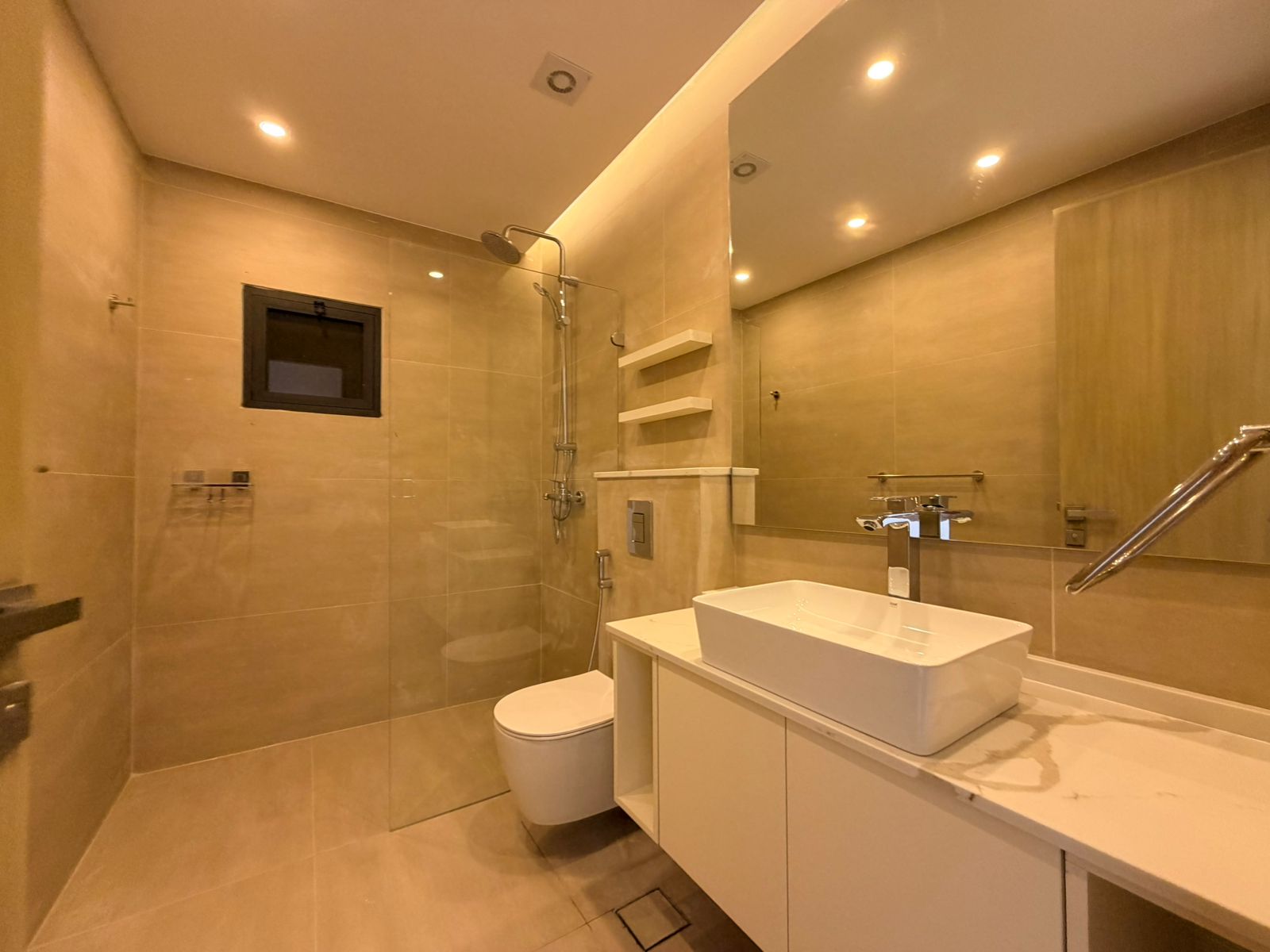 3ed5a382-6470-4f07-94e3-d86c10dec016 Modern beige-tiled bathroom with glass shower enclosure, wall-mounted toilet and white vanity sink.