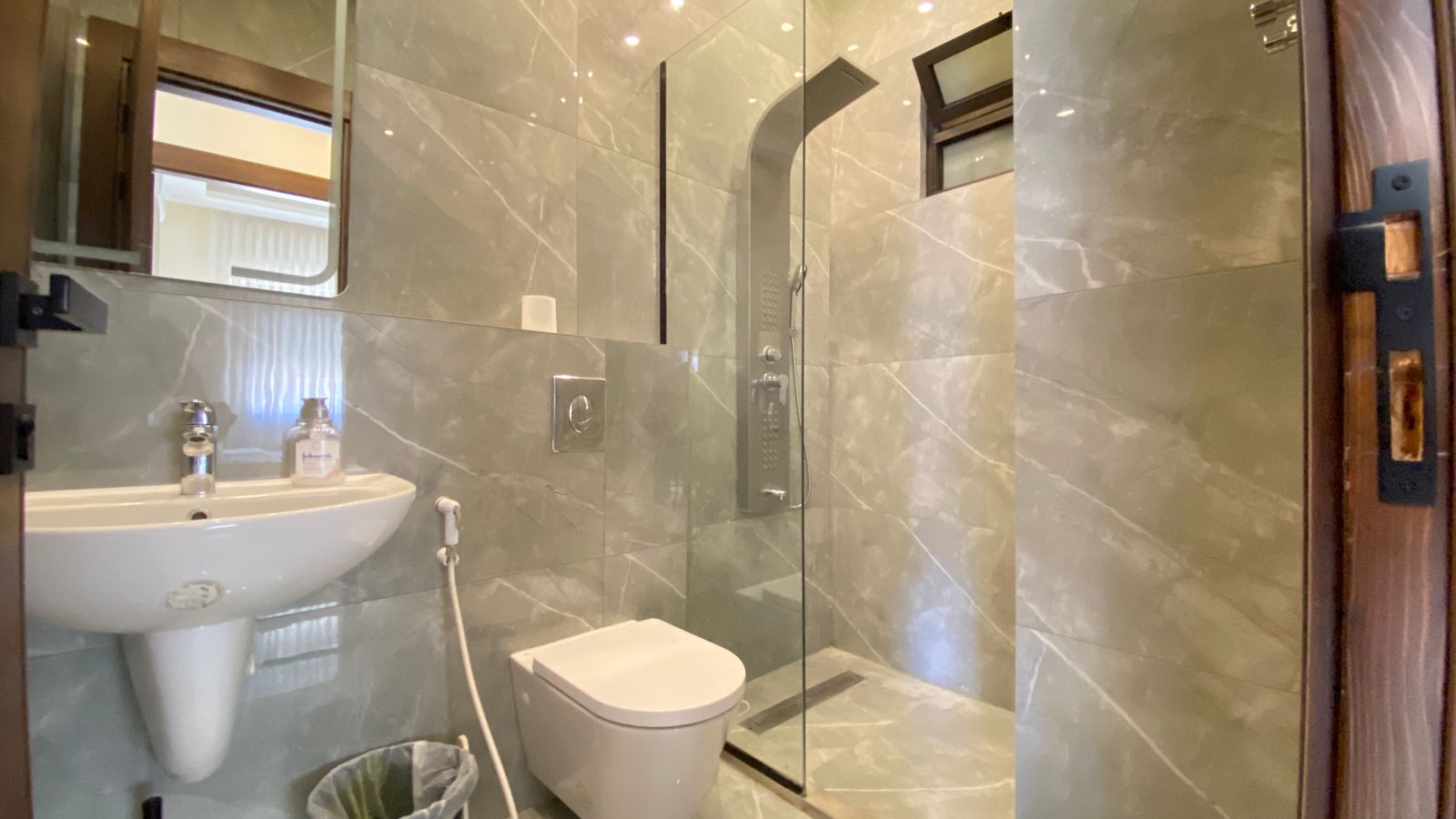 4148de88-6563-45aa-9f77-6b8034beccf8 Modern bathroom with a glass-enclosed shower, pedestal sink, and wall-mounted toilet set against grey marble walls and floor.