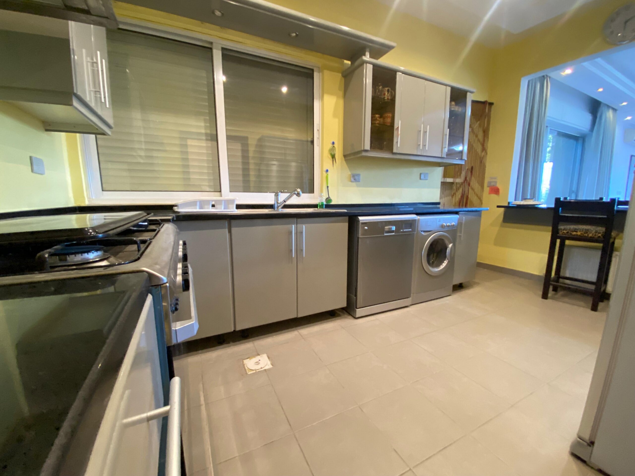 461fcd39-7265-425b-a539-559be3416578 Modern kitchen with gray cabinets, stainless steel appliances, and a washing machine along a yellow wall behind the counter that runs the length of the room.