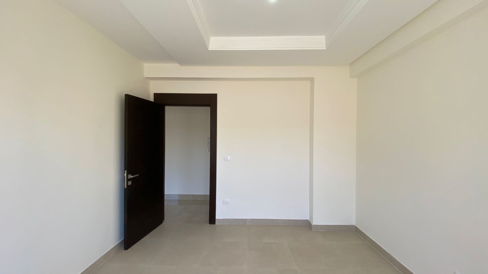 4b326352-0d5d-4f6e-8915-93bccab0c646 Empty, unfurnished room with beige tile floor, white walls, and a dark open door leading to another space.