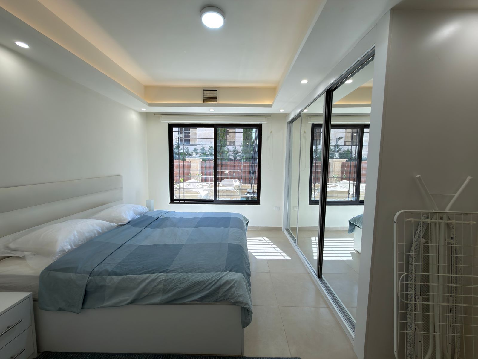 4b4b3a27-db94-4d3f-887d-00bb27abb395 Minimalist white bedroom with a low white bed, light blue bedding, and a large window with a view outside.