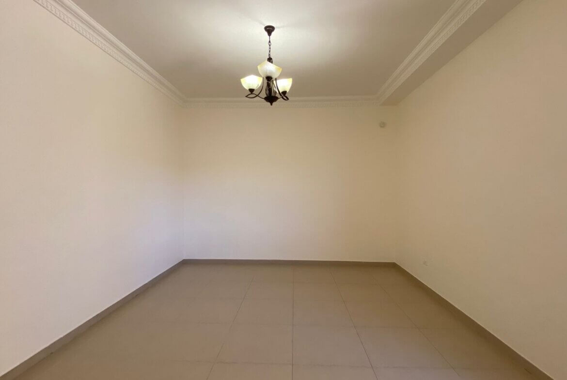4c6cb7d4-a462-4574-80d3-5d7e45a45423 Empty rectangular room with beige walls, tiled floor, and a decorative chandelier hanging from the ceiling.