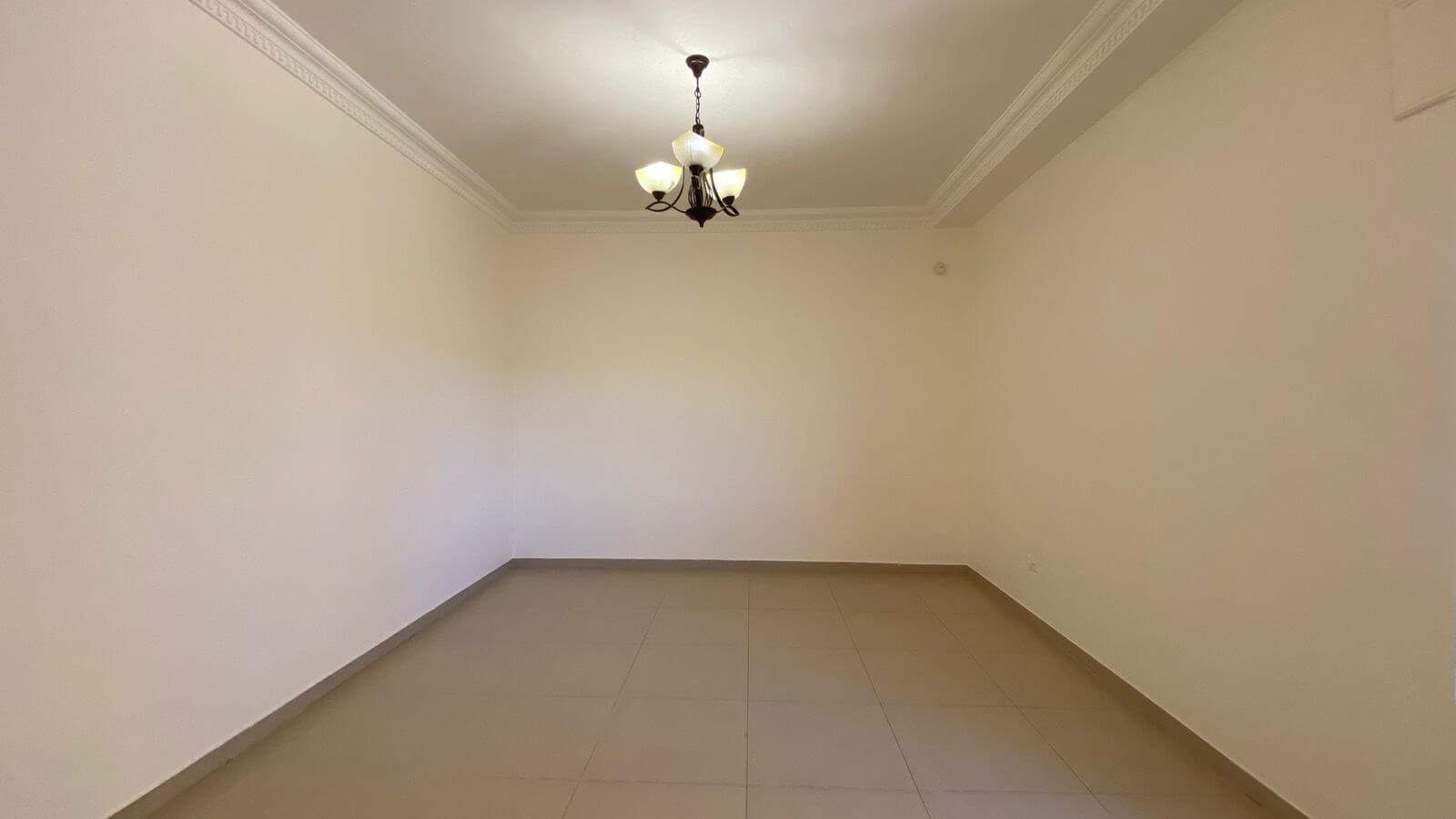 4c6cb7d4-a462-4574-80d3-5d7e45a45423 Empty rectangular room with beige walls, tiled floor, and a decorative chandelier hanging from the ceiling.
