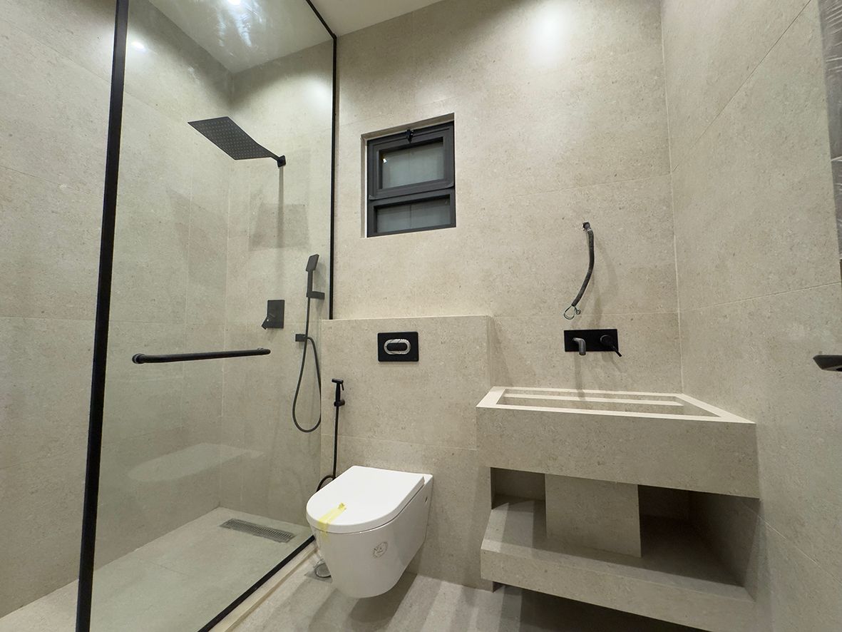 552d4857-2b37-484b-b4bd-6caf91d37439 Modern beige stone bathroom with glass-enclosed shower, wall-mounted toilet, and concrete sink counter.