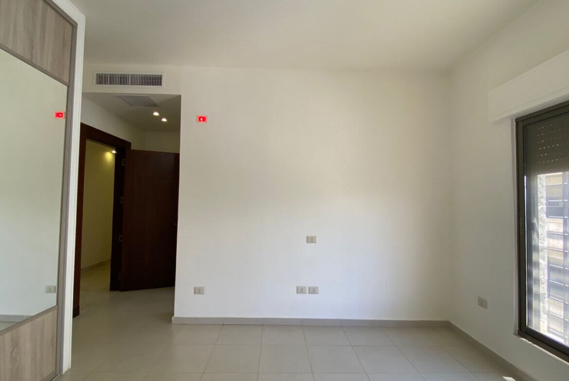 5a6dfaa0-33f1-4506-8b03-6ace1742e0fc Empty, modern room with a large window on the right, tiled floor, and a mirrored built-in wardrobe on the left.