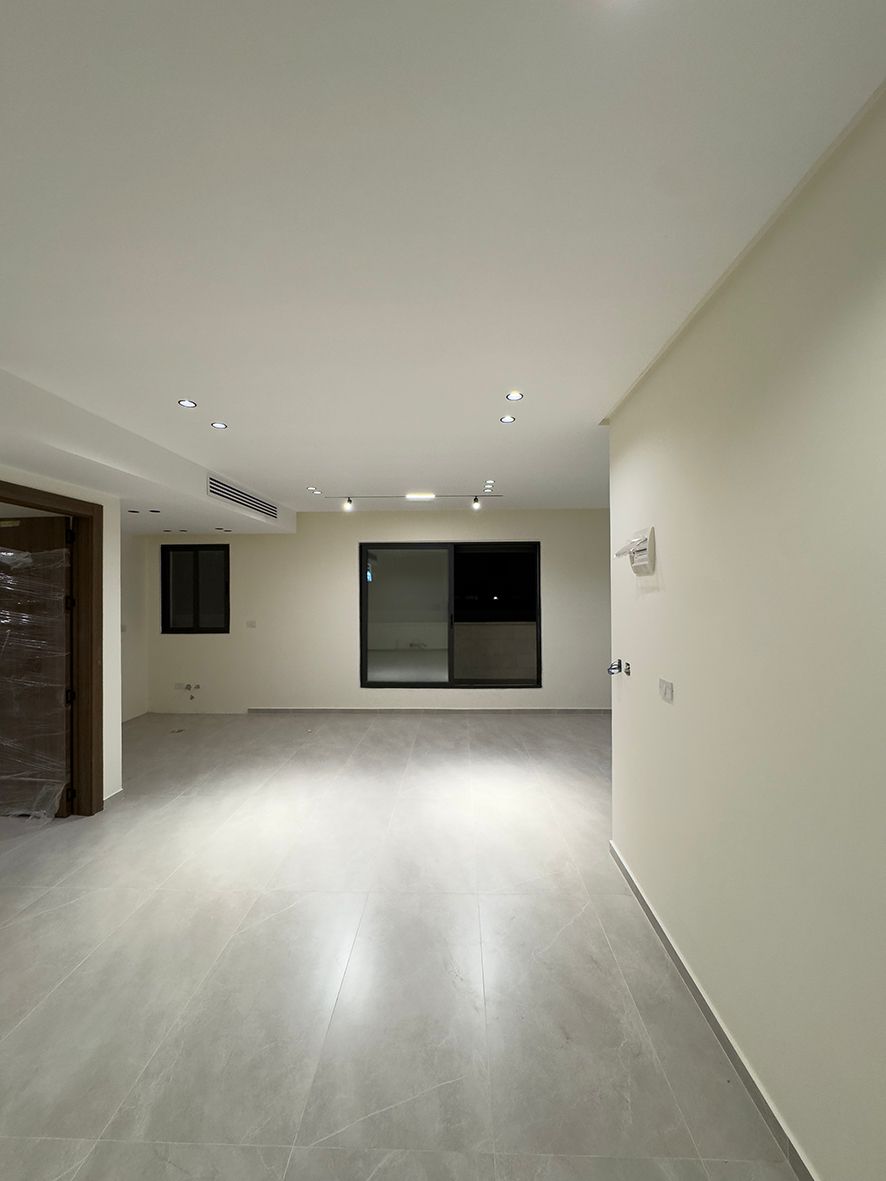 5e236e9d-ee5a-4f0d-a926-4a7efb0a3309 Empty modern living area with white walls, large window, and light gray tile floor.