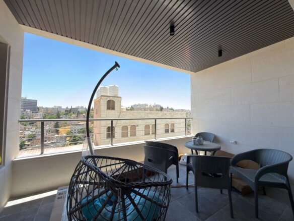 Balcony seating area with black wicker chairs and a round table overlooking a city skyline against a clear blue sky