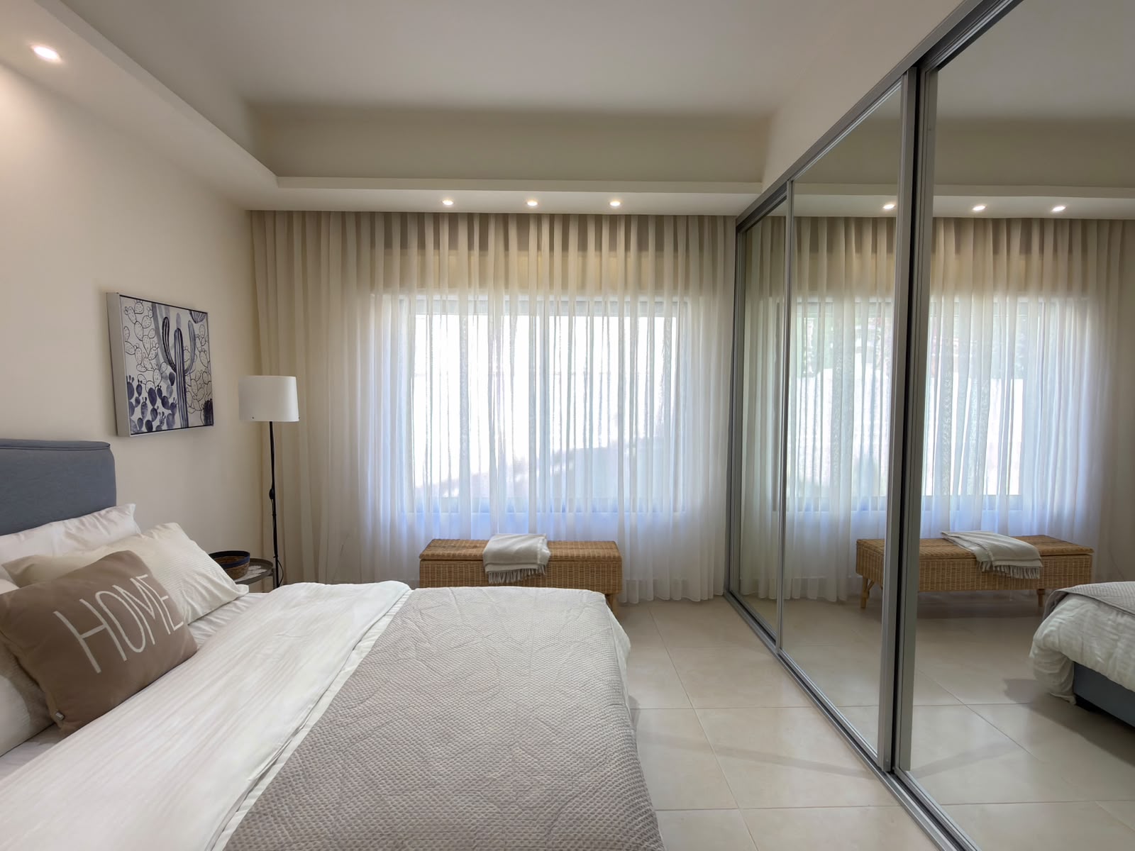 6733e808-d857-4cb0-a806-0ff1303fe31f Bright modern bedroom with a large bed, neutral bedding, sheer curtains, a wicker bench by the window, and a mirrored wardrobe door(s).