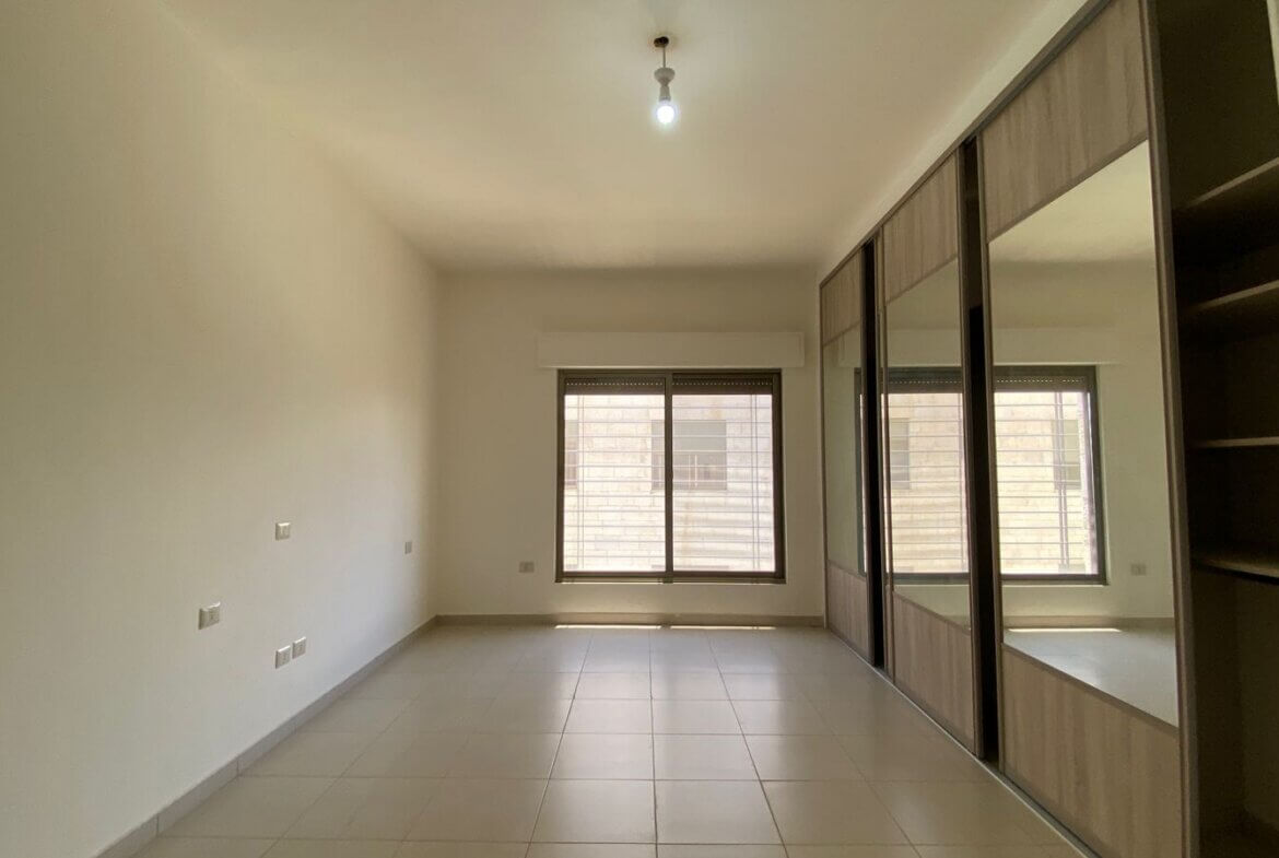 6cfbe847-b580-4d79-941f-069d23c2a67d Empty modern room with large mirrored sliding-door wardrobe along the right wall and a window at the far end