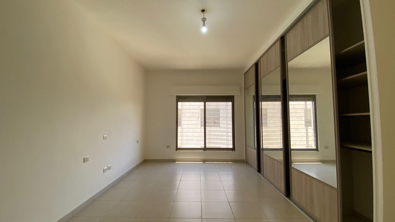 6cfbe847-b580-4d79-941f-069d23c2a67d Empty modern room with large mirrored sliding-door wardrobe along the right wall and a window at the far end