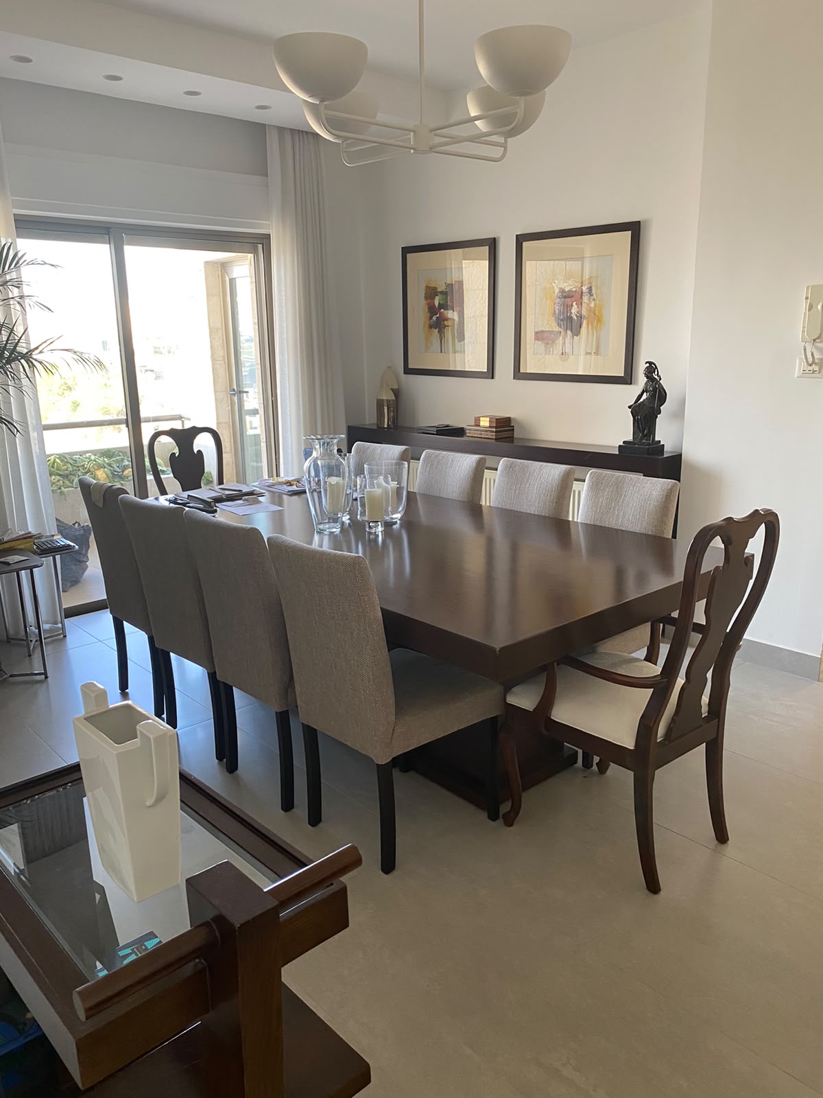 6e1ad177-ee68-485f-acce-50190ab9f37b Bright dining room with a long wooden table, beige upholstered chairs, a white chandelier, and abstract framed art on the wall.