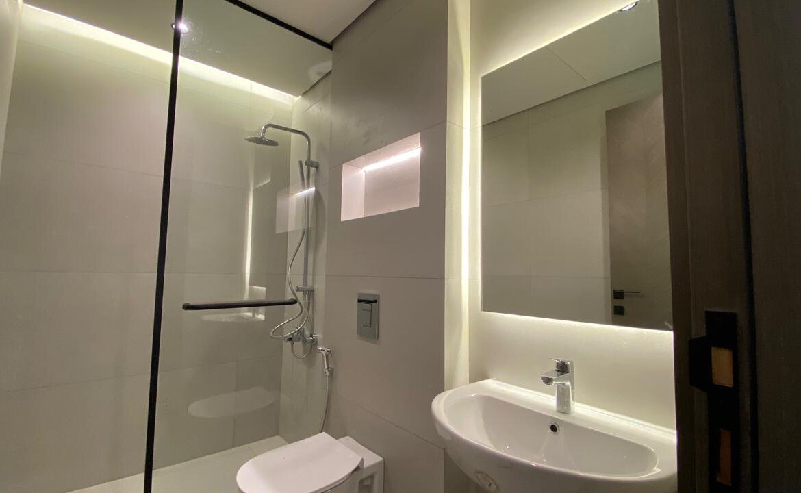 Contemporary bathroom with a glass-enclosed shower, wall niche, wall-mounted toilet, and a white sink under a backlit mirror.