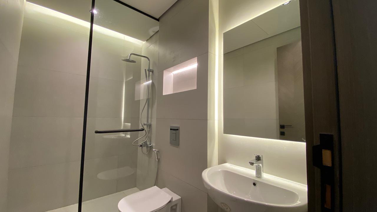 72652dd3-0b50-4a9b-bd60-7c811195a748 Contemporary bathroom with a glass-enclosed shower, wall niche, wall-mounted toilet, and a white sink under a backlit mirror.