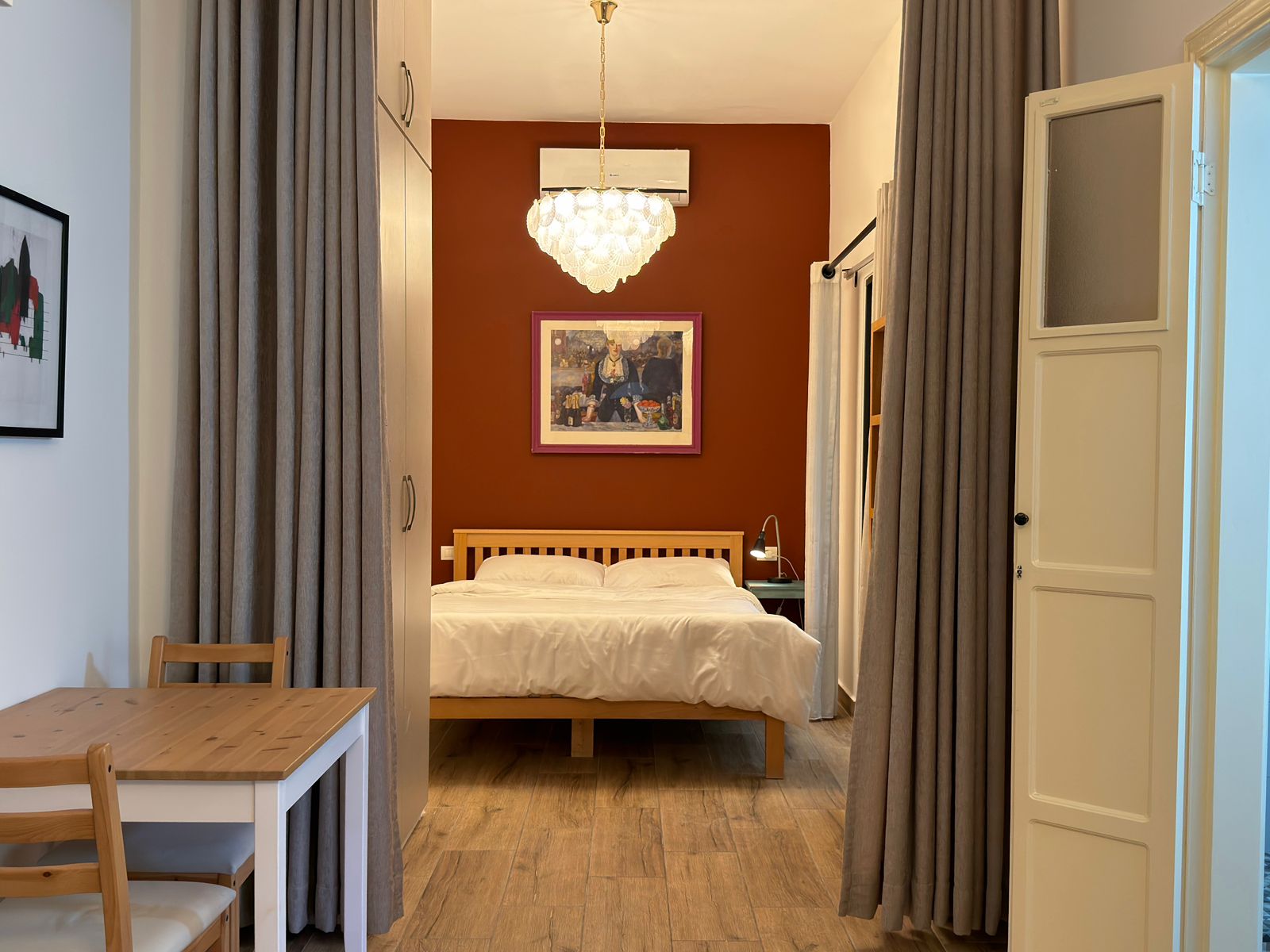 72861f88-97b6-42d0-ba3c-c994f8732e68 Bedroom viewed from the doorway with a burgundy accent wall, chandelier, framed artwork, and a wooden bed with white bedding.",