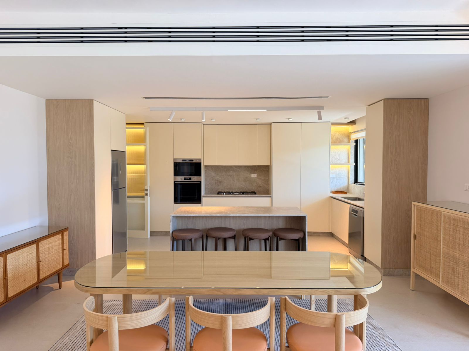 7b5c47f6-b223-4de3-a80c-edecdd78f08c Modern, open-plan kitchen with white cabinets, a central island with five brown stools, and built-in ovens.