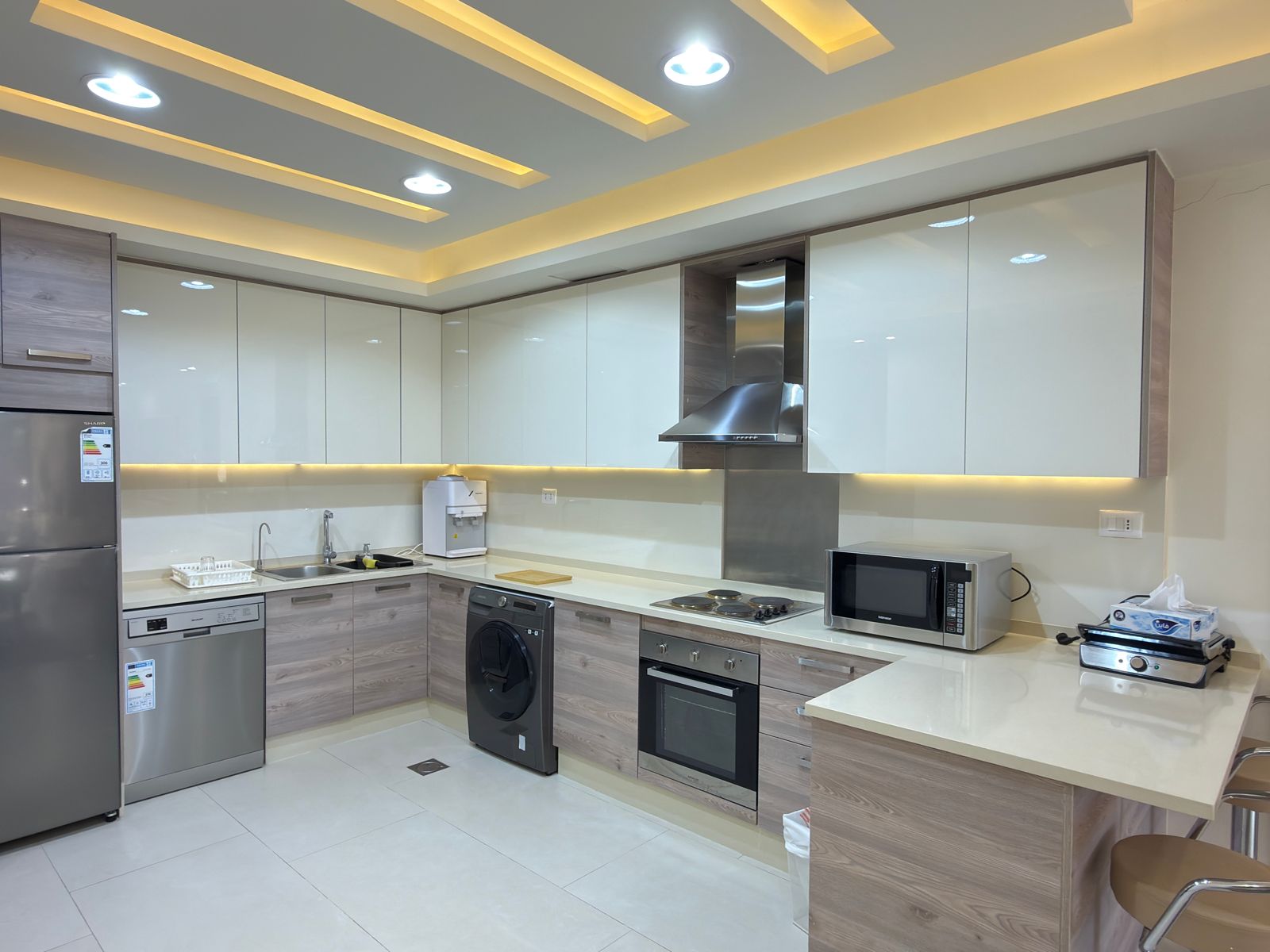 7d9e4f78-076d-4e54-ad50-5e7591f078e3 Modern U-shaped kitchen with white glossy upper cabinets, wood-grain lower cabinets, and under-cabinet lighting.