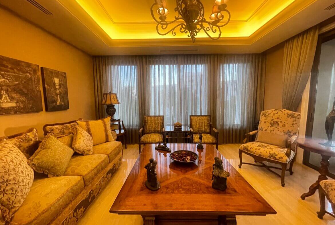 7e61f1d1-bc28-456b-bf8e-4882c266c522 Luxurious living room with an ornate chandelier, beige floral sofa, and patterned armchairs facing a wooden coffee table.