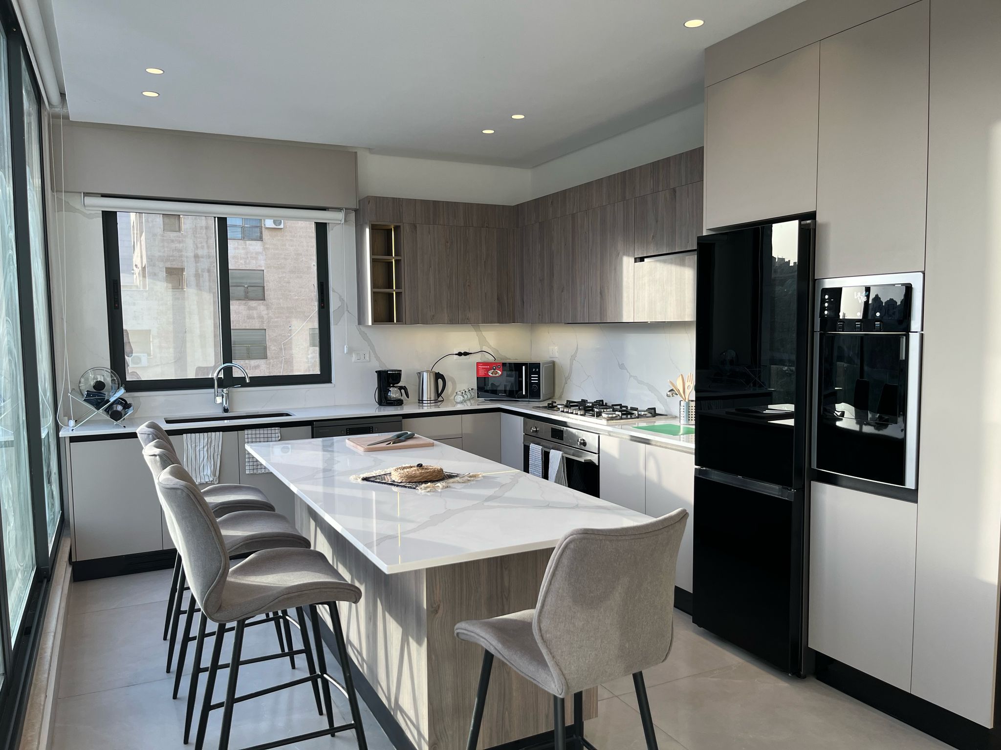 83be408f-e085-40a6-b737-e72c48114d40 Modern kitchen with a marble island, light wood and gray cabinets, and stainless steel appliances