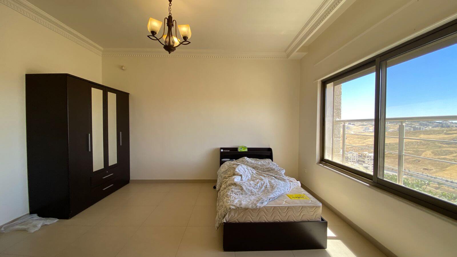 85546a56-23a2-4b67-b8ad-ca91a61d2f06 Bedroom with a single bed near the window, a dark wardrobe on the left, and natural daylight filling the room.