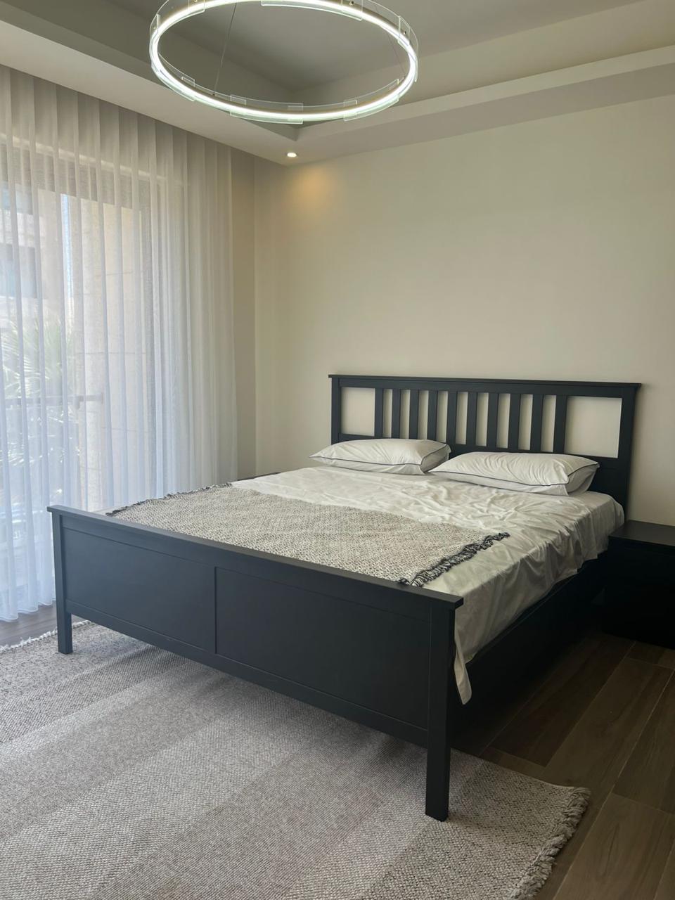 864f5f54-3381-499a-9695-fd22c4a81c7b Dark gray wooden bed frame with white bedding and two pillows in a minimalist bedroom.