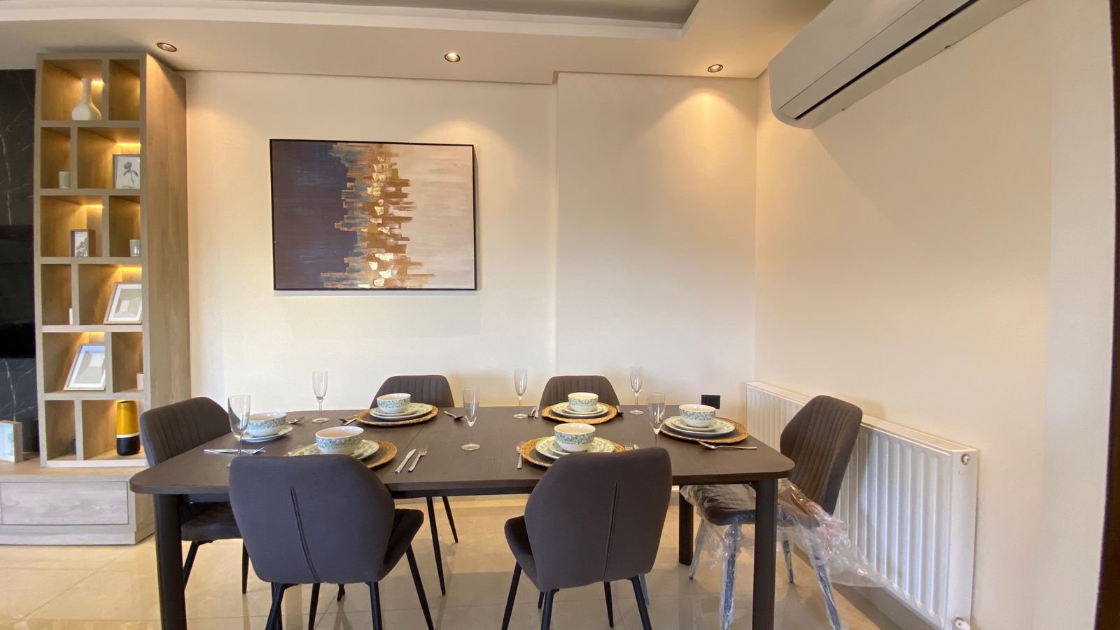 8801437e-e40b-4e16-921e-91c64469fdad Dining room with a dark wooden table set for six, plates, bowls, and wine glasses in a modern space.