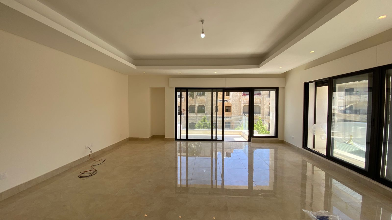 89746d27-abb6-4a54-bbb2-2181e03a4475 Empty modern living room with glossy tile floor, recessed ceiling, and large sliding glass doors to a balcony.