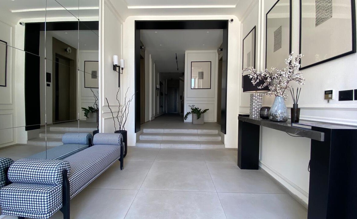 Modern white lobby with a black-accented console table on the right and a checkered upholstered bench in the foreground.