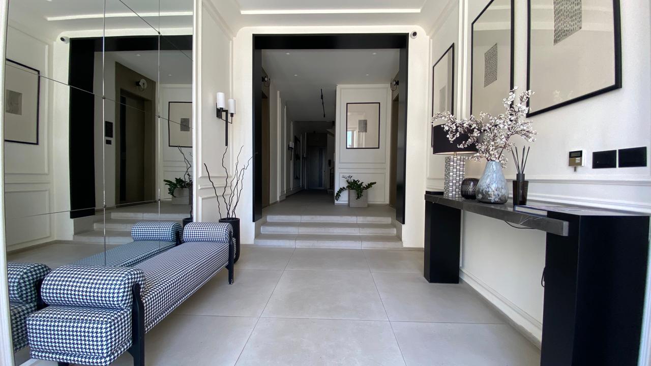 8a3c8353-00be-43bd-9117-26f25438acb5 Modern white lobby with a black-accented console table on the right and a checkered upholstered bench in the foreground.