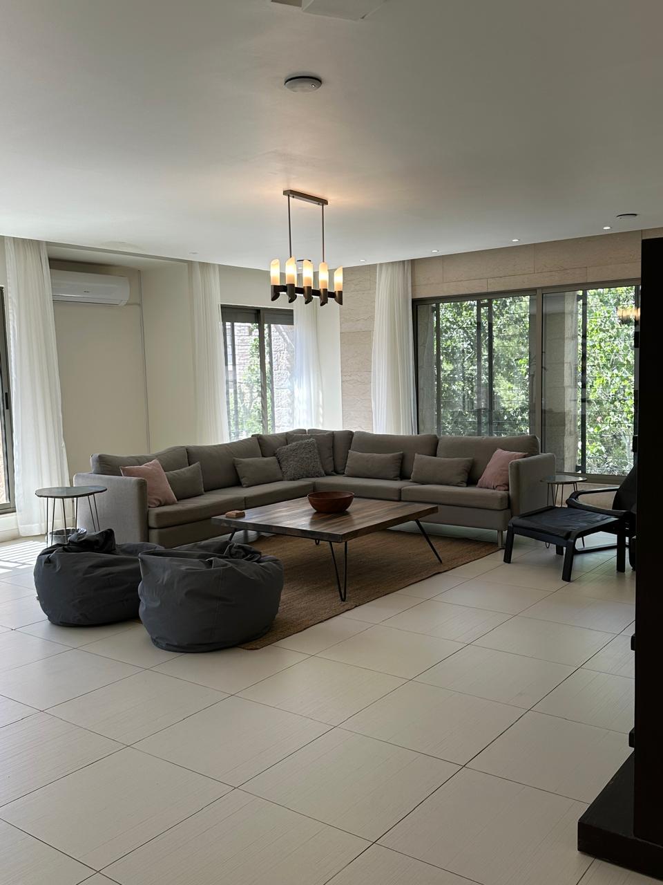 9013ee59-b0b1-4aed-9d85-79c40863d900 Bright living room with an L-shaped gray sectional, throw pillows, two gray bean bags, a wooden coffee table, and a rug. (Note: Informative image)