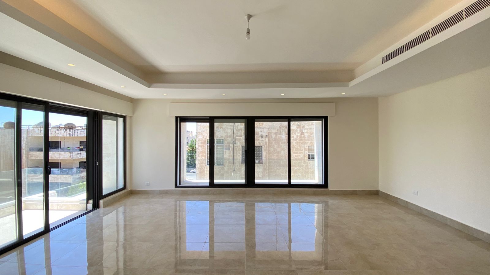 95da4b2f-20b5-4d61-9362-fa689633a3df Bright living room with large black-framed sliding glass doors to a balcony, polished beige tile floor, and a recessed ceiling with lights.
