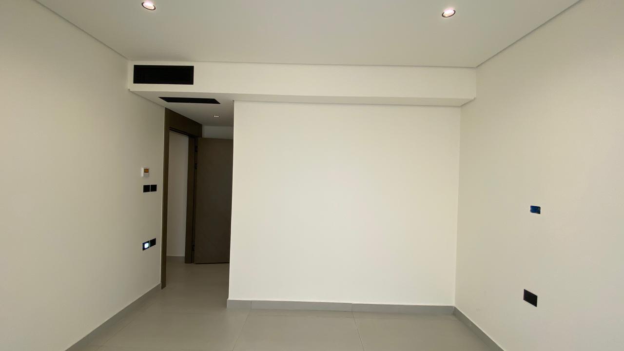 96f48303-a7a9-4f88-b44f-bcae485cd3c6 Empty white interior room with a doorway on the left, a partial central wall, and recessed ceiling lights above.