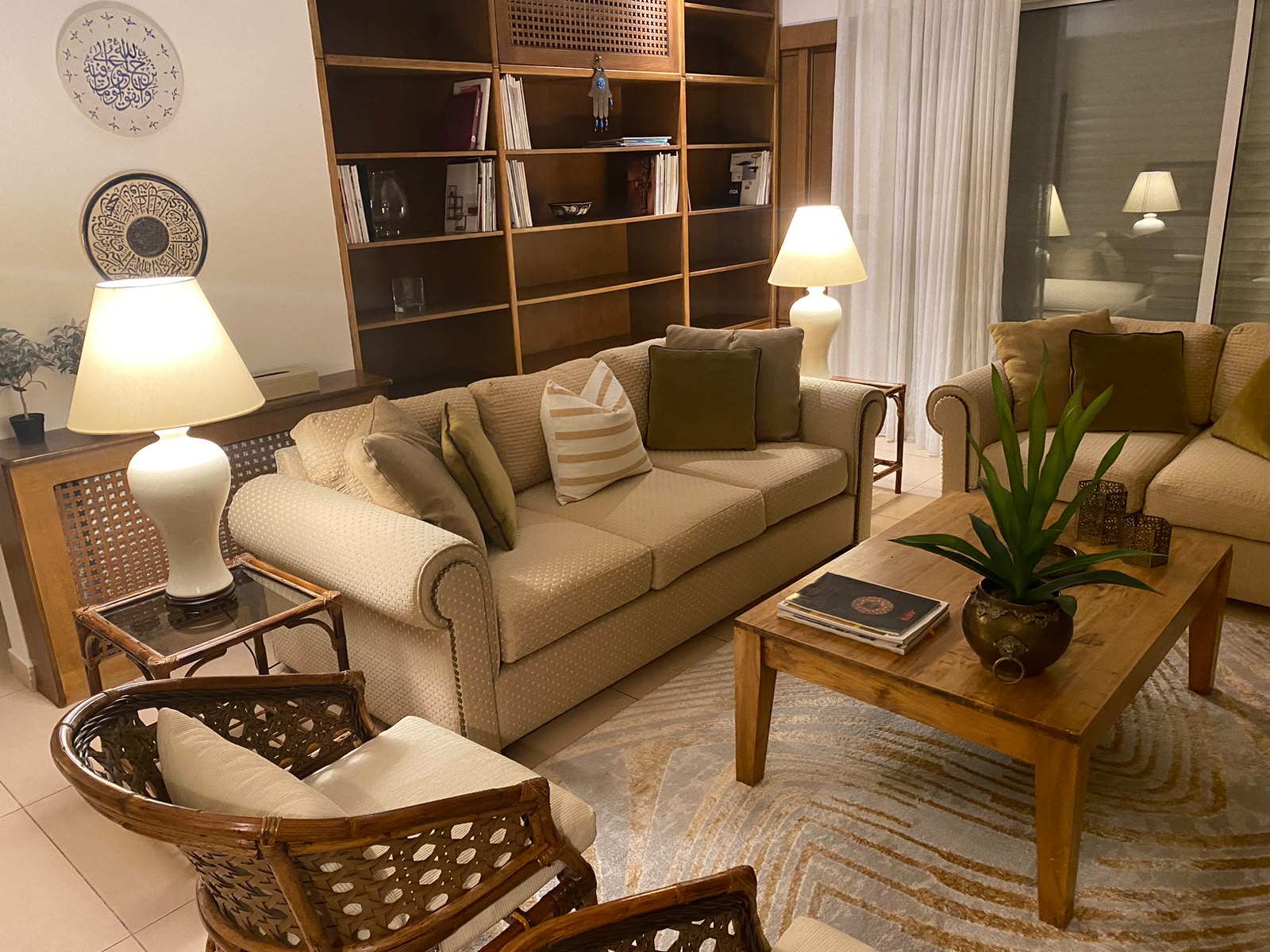 990c87aa-91ec-40a8-a4f5-c334a3b9f98e Cozy living room with beige upholstered sofas, striped pillows, and a wooden coffee table with a potted plant and magazines.