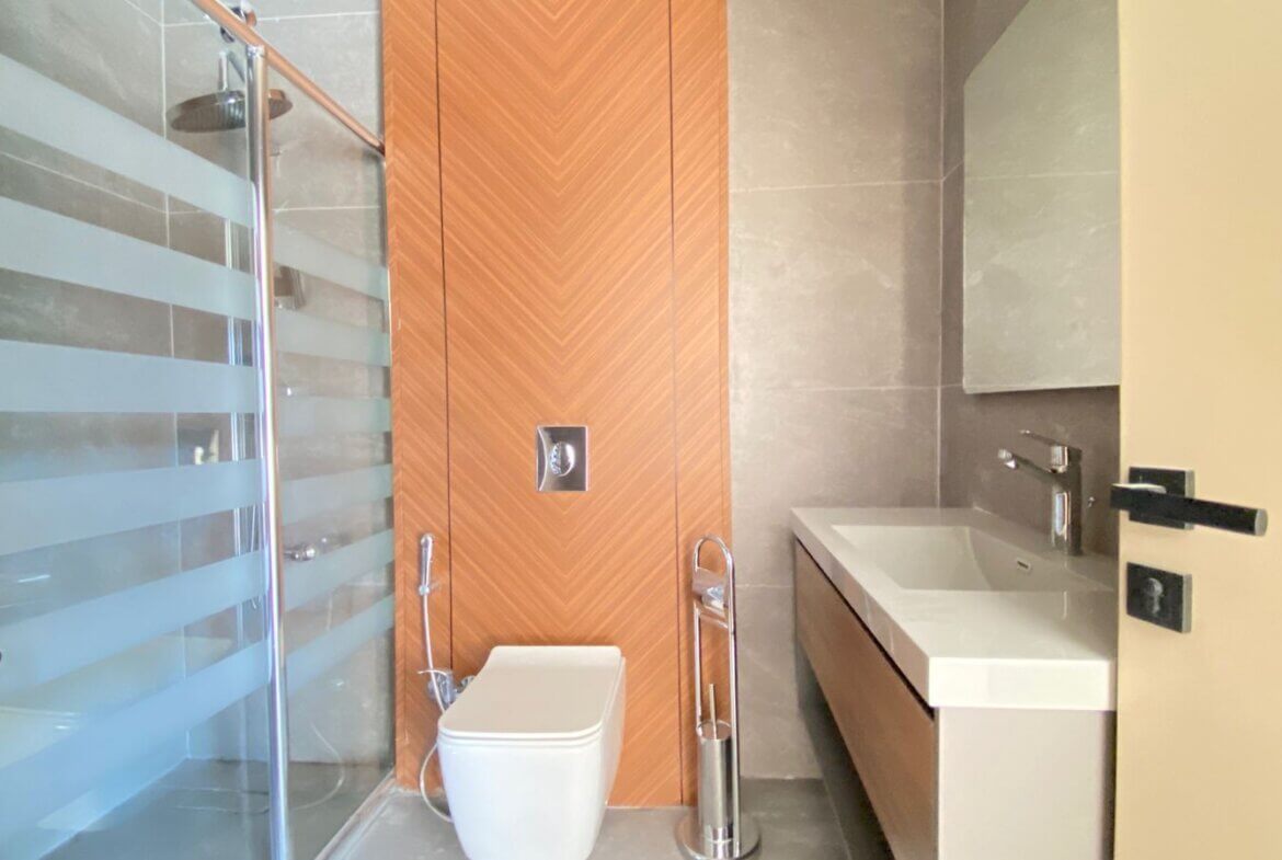 Contemporary bathroom with glass shower enclosure, striped frosted glass, and a wood chevron panel behind a wall-mounted toilet.