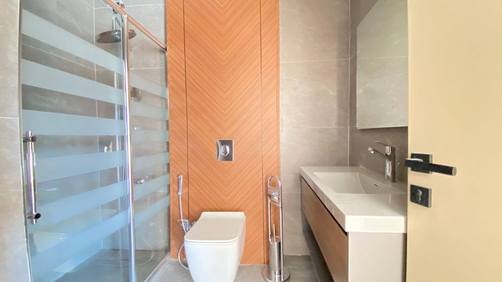 Contemporary bathroom with glass shower enclosure, striped frosted glass, and a wood chevron panel behind a wall-mounted toilet.
