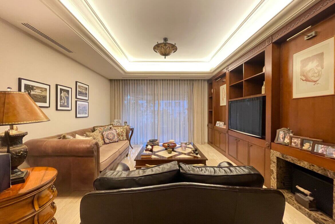 a006c35f-512a-45fc-ab1d-74806f46da2f Cozy living room with brown leather sofas, a wooden coffee table, and built-in wooden shelves with a TV along one wall.