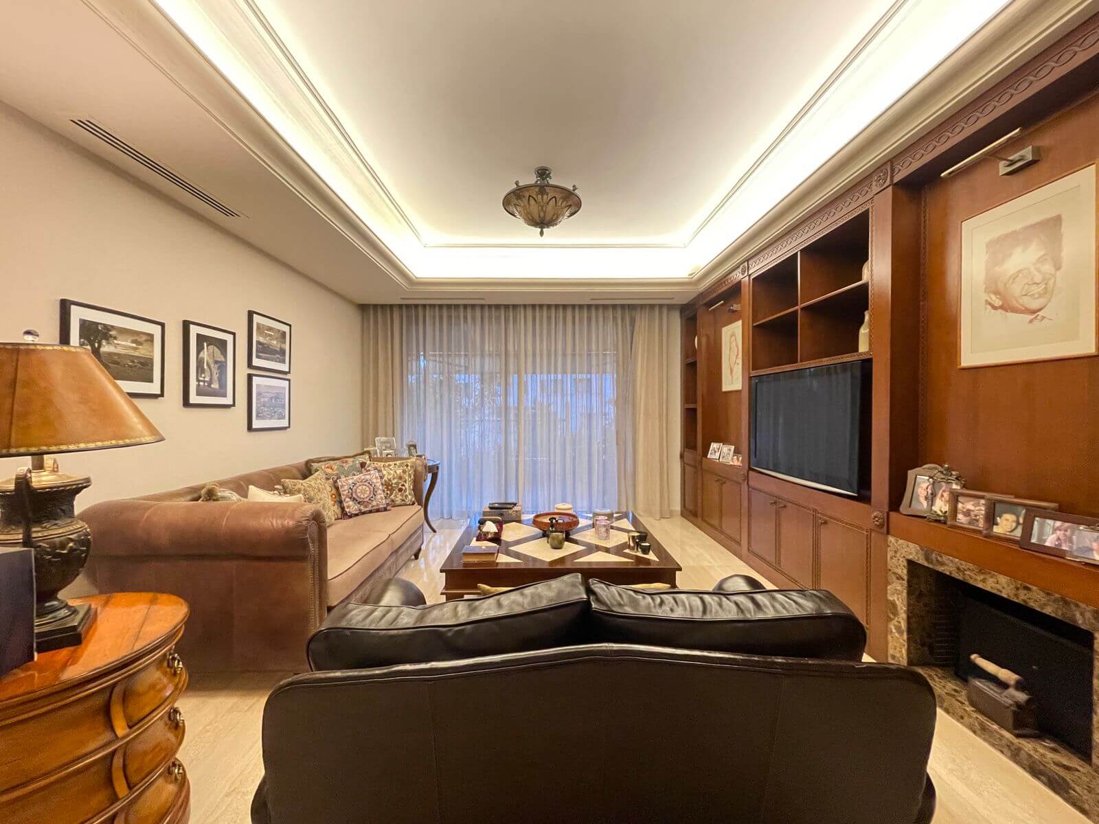 a006c35f-512a-45fc-ab1d-74806f46da2f Cozy living room with brown leather sofas, a wooden coffee table, and built-in wooden shelves with a TV along one wall.