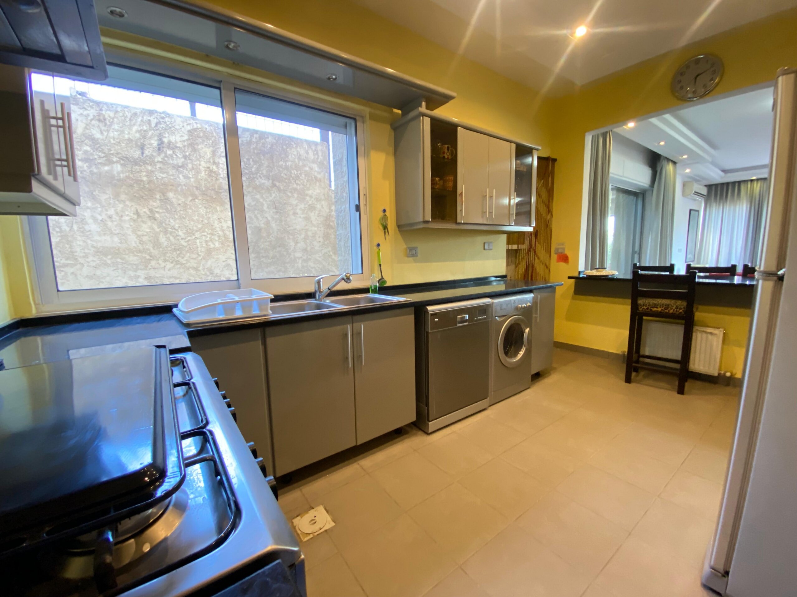 a056cd01-fe95-460a-85de-ef036ac2a85b Bright kitchen with yellow walls, gray cabinets, and a stainless-steel stove and sink by a large window.