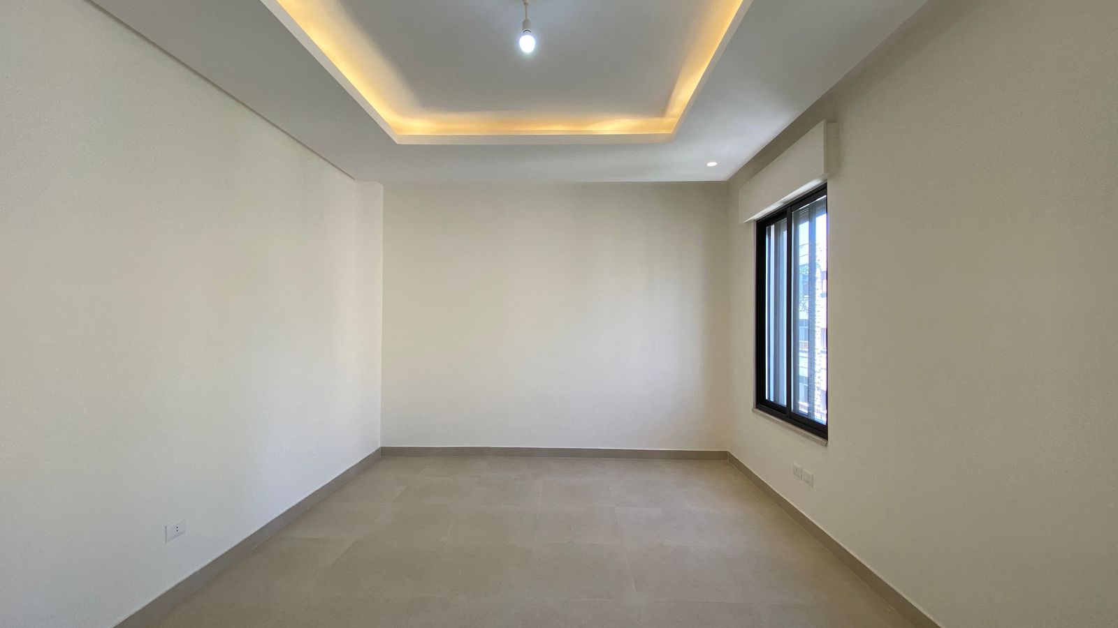 a8a3d998-92bb-45db-9681-530cd8ac6cee Empty modern room with white walls, beige tiled floor, and a large window on the right; recessed ceiling lights.