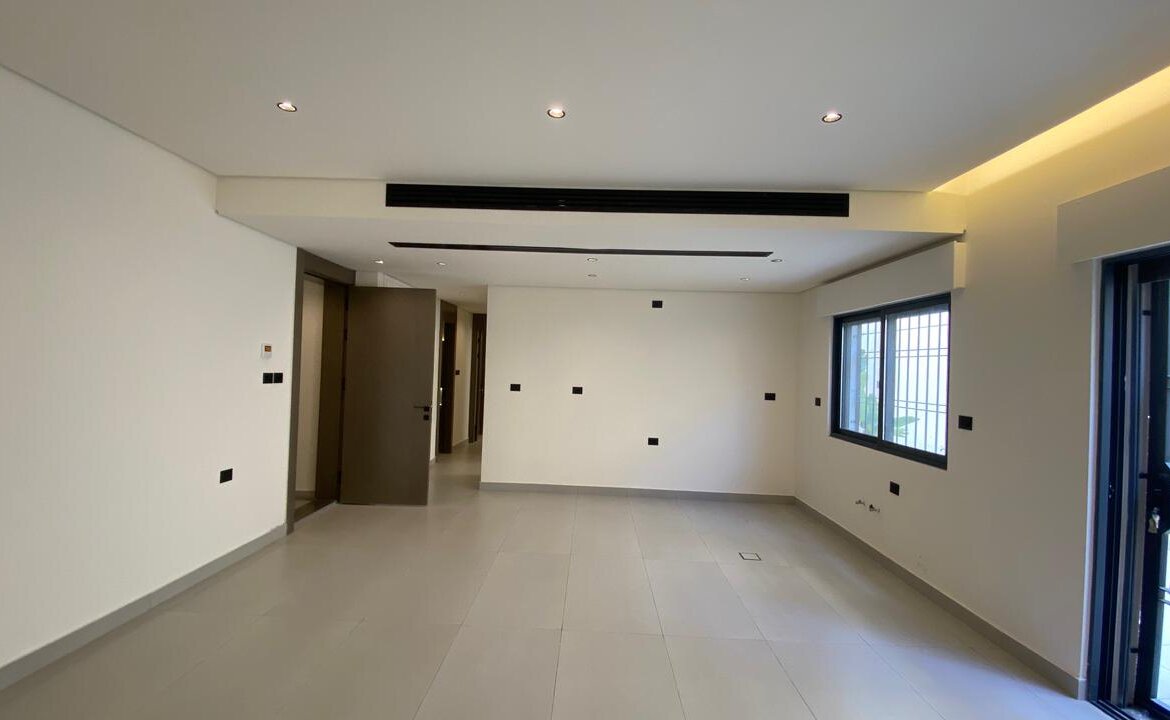 Empty modern living room with gray floor tiles, white walls, recessed ceiling lights, a large window and balcony door