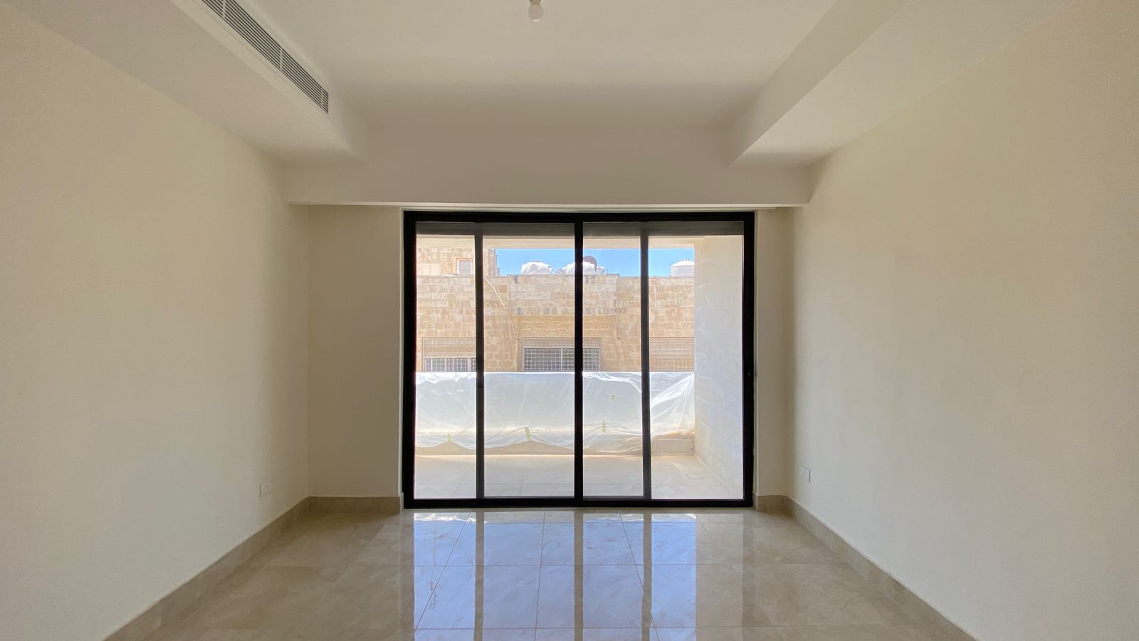 ac4c0a10-6f55-411d-ac46-e6693533f3cd Empty modern room with large floor-to-ceiling sliding glass doors opening to a balcony, beige tiled floor and white walls.